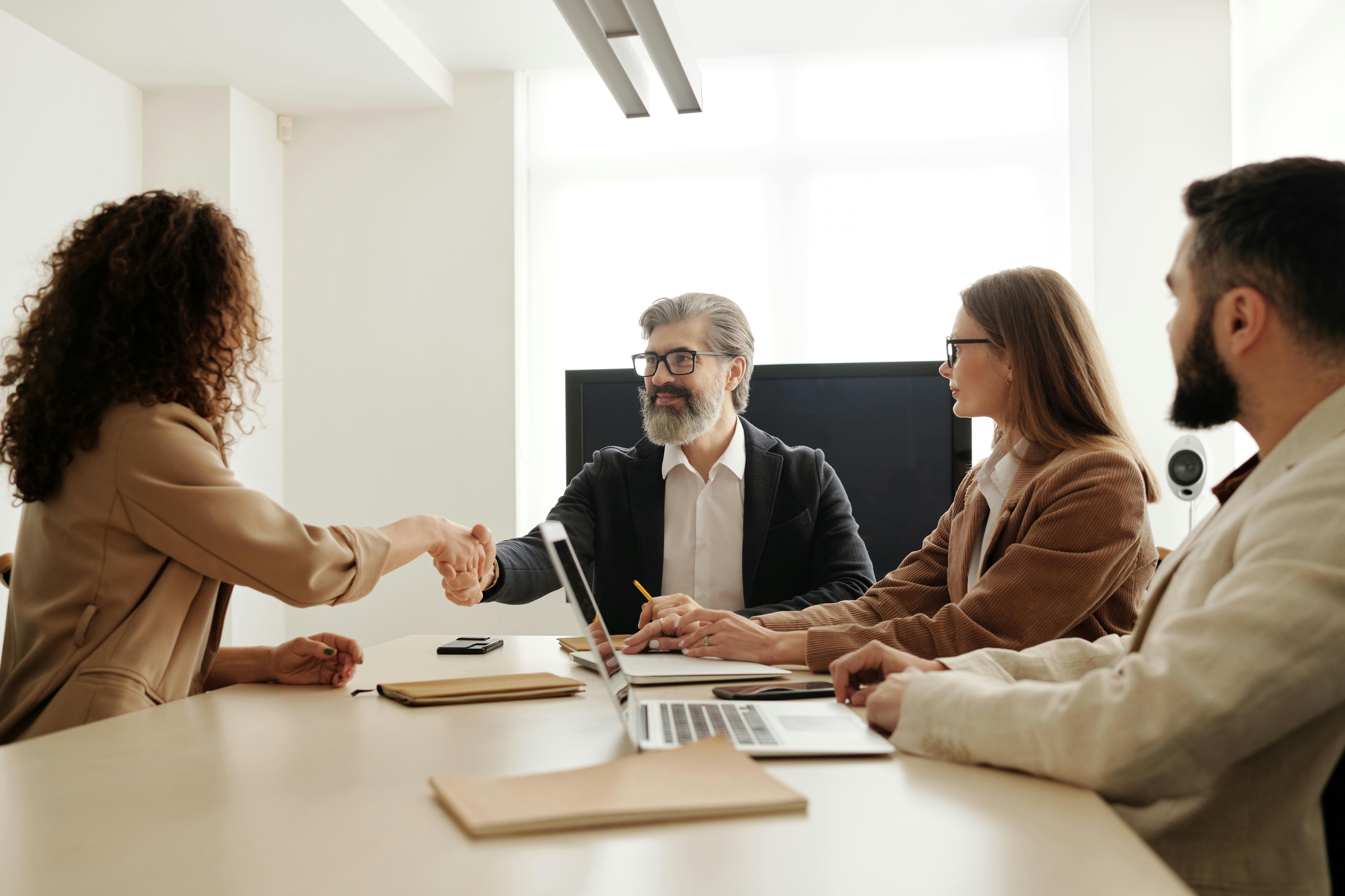 An illustration of a professional recruitment process, featuring a diverse group of candidates and a recruiter shaking hands. Symbolizing job interviews, candidate evaluation, and selection.